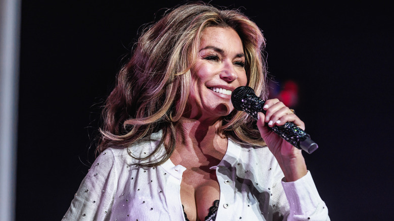 Shania Twain performing in a white top and lacy black bralette.