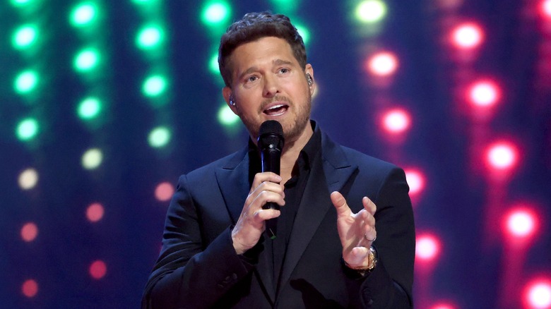 Michael Bublé wearing a black jacket and black collared shirt while holding a microphone