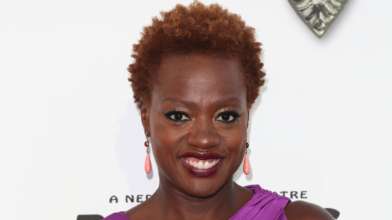 Viola Davis wearing her natural hair while wearing a purple strapless dress and peach colored drop earrings