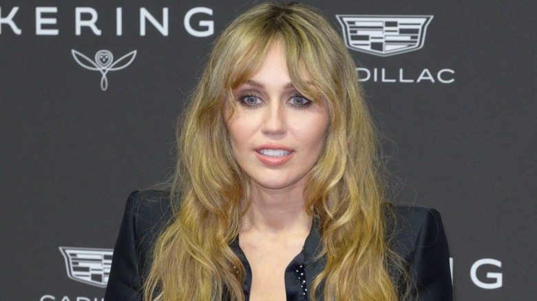 Wearing a black number, Miley Cyrus looks into the camera while smiling