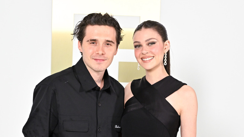 Wearing black outfits, Brooklyn Beckham and Nicola Peltz smile at the camera.