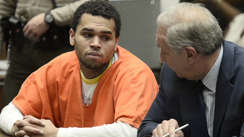 Chris Brown in an orange jumpsuit, sitting at table in court with his lawyer